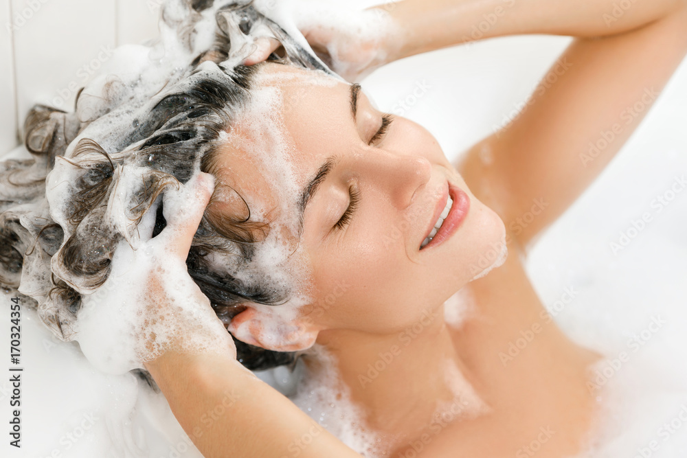 Woman is washing her hair with shampoo - obrazy, fototapety, plakaty 