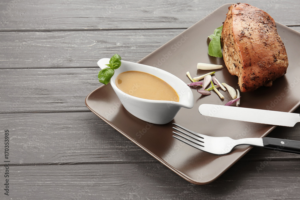 Plate with turkey gravy in sauce boat and baked meat on table
