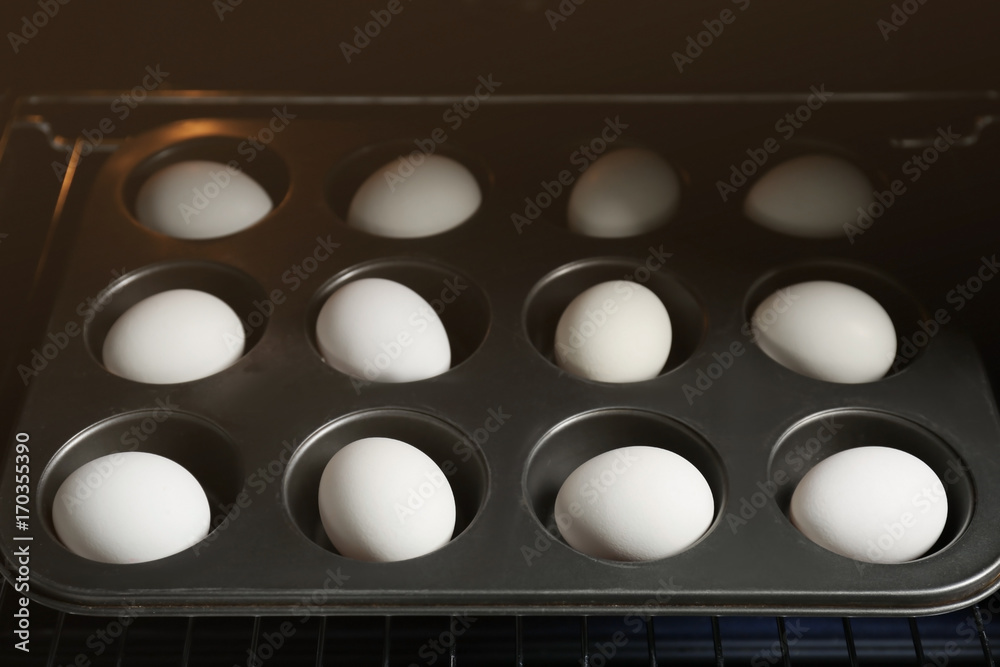 Muffin tin with hard boiled eggs in oven, closeup