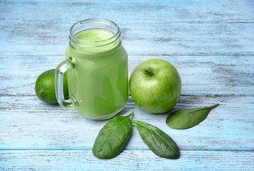 Mason jar of green healthy juice with fruits on wooden table