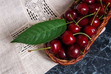 Fresh organic cherry and big green leaf in yellow wooden basket on dark marble background..