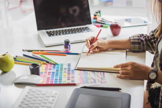 Young asian female designer using graphics tablet while working with computer at studio or office.
