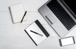 © mirage_studio - Top view on white wooden table with open laptop computer, blank cell phone, empty diary and graphic tablet, free space. Mobile phone with white screen, copy space