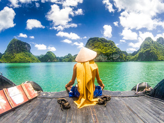 Wall Mural - man wearing a Vietnamese hat enjoying the magnifiecent sight of Ha Long bay limestone rocks on a beautiful sunny day during a boat cruise, Vietnam