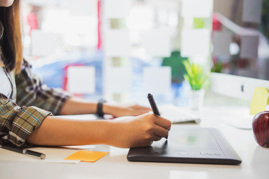 Young asian female designer using graphics tablet while working with computer at studio or office.