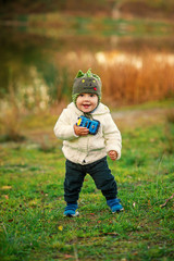 Wall Mural - A little funny boy with two teeth in warm clothes playing near the lake on the sunset.