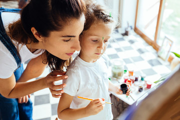 Wall Mural - Happy family. Mother and daughter dressed in white shirt and blue jeans together paint. Adult woman helps the child girl. Top view. New housing, art and family leisure concept.