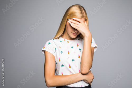 Fotomural Portrait of young scared woman covering eyes with hands while standing against gray studio background