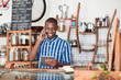 © mavoimages - Smiling young African entrepreneur busy working in his cafe