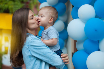 portrait of young beautiful mother kissing her baby boy on balloons background