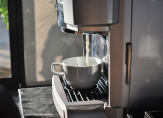 Wall Mural - Fresh coffee drops falling to white cup, coffee machine preparing white cup of coffee