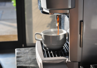 Wall Mural - Fresh coffee drops falling to white cup, coffee machine preparing white cup of coffee