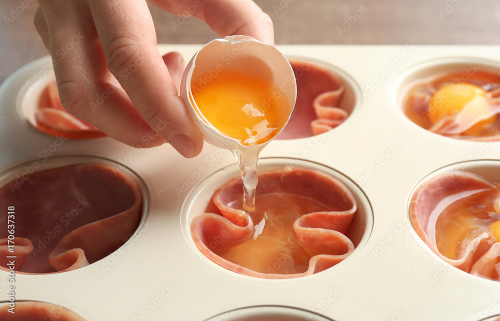 Woman adding egg into muffin tin with ham, closeup