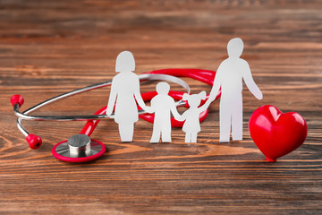 Poster - Paper silhouette of family, stethoscope and heart on wooden background. Health insurance concept