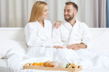 Wall Mural - Tray with breakfast in hotel room and happy young couple on background