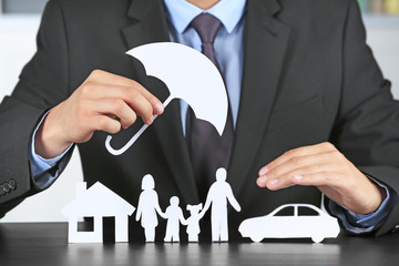 Poster - Man holding umbrella over paper silhouette of family, house and car on table. Insurance concept