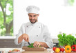 Young male chef cutting salad leaves in kitchen