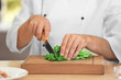 Male chef cutting salad leaves on table, closeup