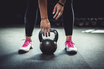 Woman in gym reaching for a kettlebell, with chalked hands. Authentic mood.