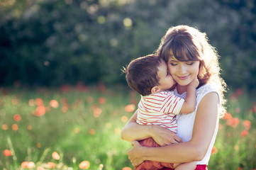 young beautiful happy mother with her little 2 year old son in field of poppies in the sun. summer.