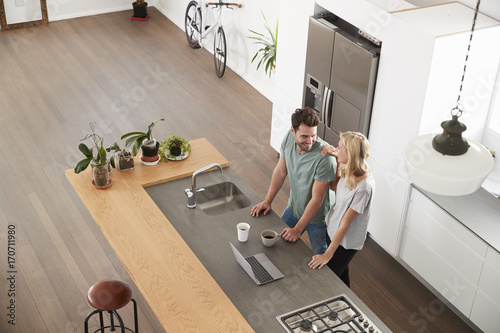 Fotografie, Obraz Overhead View Of Couple Looking At Laptop In Modern Kitchen