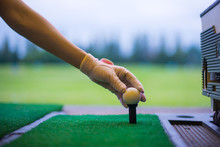 Woman Golfer's Hand Holding Ball On Tee With Golf Course Background. Close Up Of Golf Players Hand Placing Ball On Tee At Driving Range In Sport Club.