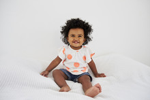 Portrait Of Smiling Baby Girl Sitting On Bed