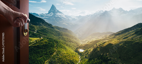 Photographie hand opens empty room door to nature and mountains