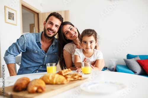 Zdjęcie XXL Mąż i żona z nimi mała córka siedzi przy stole w kuchni. Portret rodzinny.