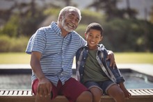 Smiling Grandfather And Grandson Sitting Together On Bench