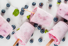 Summer sweets and desserts. Vegan food. Frozen drinks, smoothies. Ice cream popsicles from homemade Greek yogurt and fresh organic blueberries. With mint. On white marble table. Copy space top view