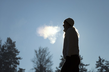 Silhouette of a woman with hat breathing warm air during a cold winter morning. Selective focus used.