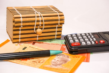 Brown small gift box and Malaysian currency notes with calculator and ballpen on white floor