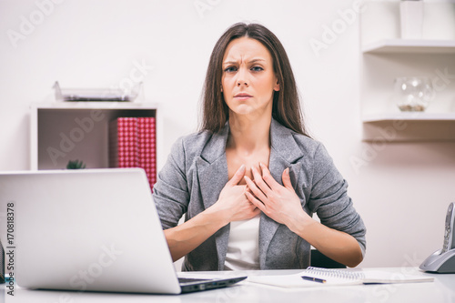 Plakat Młoda businesswoman ma ból w klatce piersiowej w pracy.