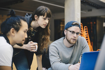 Male and female computer programmers using laptop at desk in office