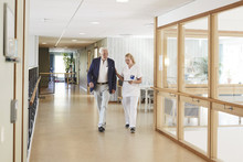 Full Length Of Female Nurse And Senior Male Patient Walking In Hospital Corridor