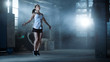 Athletic Beautiful Woman Exercises with Jump / Skipping Rope in a Gym. She's Covered in Sweat from Her Intense Cross Fitness Training. Dark atmosphere.
