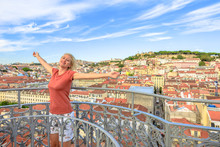 Happy Tourist Woman With Open Arms At Elevador De Santa Justa In Lisbon, Portugal. Monastery Of Sao Vicente Of Fora And Sao Jorge Castle On Background. Blonde Female Enjoys At Popular Landmark.