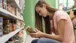 © alexeg84 - Woman picking canned food from the shelves at supermarket and reading the label