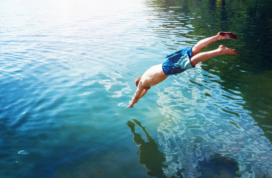 Fototapete - man jumps like fish into the water of the lake, swims, enjoys spending time on summer holidays