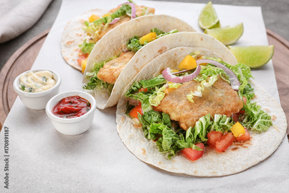 Wooden board with delicious fish tacos on kitchen table