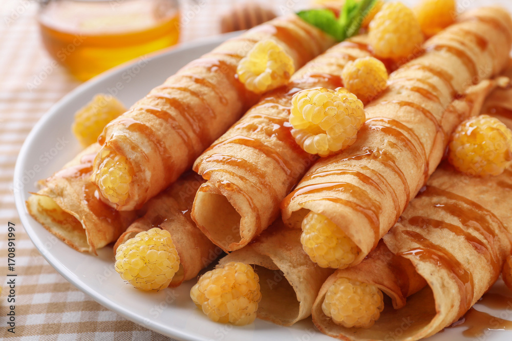 Rolled thin pancakes served with yellow raspberry on white plate