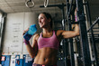© ADDICTIVE STOCK - Young woman drinking from bottle while posing in gym