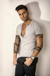 © theartofphoto - Handsome tattooed young man wearing grey t-shirt, standing against light background in studio shot