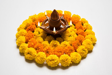 flower rangoli for Diwali or pongal or onam made using marigold or zendu flowers and red rose petals over white background with diwali diya in the middle, selective focus
