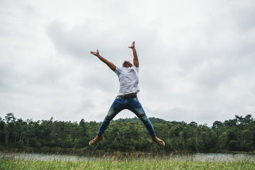 Asian man travel relax in the holiday. Jump on a green pasture.