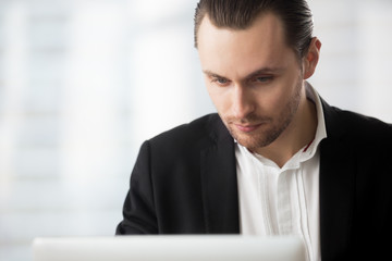 Wall Mural - Smart young businessman in dress suit sitting in office, looking at laptop screen with thoughtful expression, contemplating an important project or looking for information concept. Close up portrait