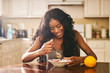 Smiling young woman eating breakfast at table in kitchen