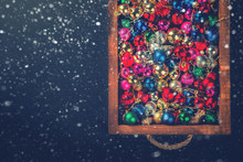 Christmas Toys,Colored Balls In A Wooden Box On A Black Background.Toned Image.Vintage Style.  Top View. Selective Focus.New Year Christmas Card. Drawn Snowfall