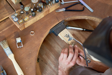 Wall Mural - High angle closeup of jeweler making flower ring in workshop, forming  it on work station with different tools